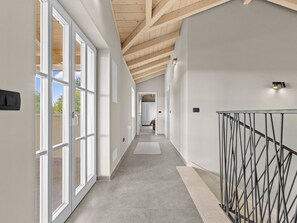 A modern interior with a hallway leading to a room, featuring a wooden ceiling, large windows, and a metal railing. - Villa Lunistra by Interhome (Cere)