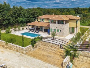 Une maison à deux étages avec une piscine, des murs en pierre et un jardin.