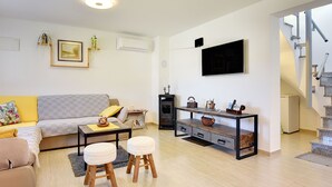 Ett modernt vardagsrum med en soffa, ett soffbord, pallar, en öppen spis, en tv och en trappa.