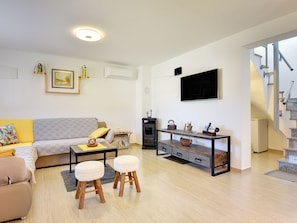 Ein modernes Wohnzimmer mit einer Couch, einem Couchtisch, Hocker, einem Kamin, einem Fernseher und einer Treppe.