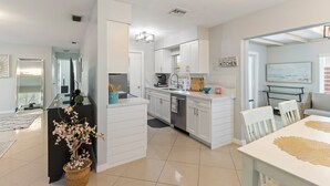 Een moderne keuken met witte kastjes, een eethoek met tafel en stoelen, en een woonkamer met een bank en salontafel.