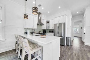 A modern kitchen with white cabinetry, a central island, stainless steel appliances, and pendant lighting. - The Magnolia by Stay on 30a (Inlet Beach)