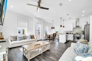 A spacious living area with a sofa, coffee table, and dining table, connected to a kitchen with modern appliances and a ceiling fan. - The Magnolia by Stay on 30a (Inlet Beach)