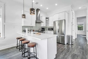A modern kitchen with white cabinetry, stainless steel appliances, and a central island with stools. - The Azalea by Stay on 30a (Inlet Beach)