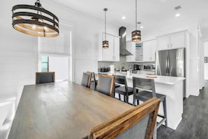A modern kitchen with white cabinets, stainless steel appliances, and a wooden dining table. - The Jasmine by Stay on 30a (Inlet Beach)