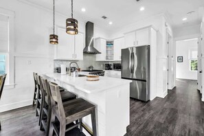 A modern kitchen with white cabinetry, a central island, stainless steel appliances, and pendant lighting. - The Jasmine by Stay on 30a (Inlet Beach)