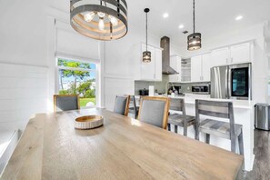 A modern kitchen with white cabinetry, a wooden dining table, and pendant lighting. - The Lily by Stay on 30a (Inlet Beach)
