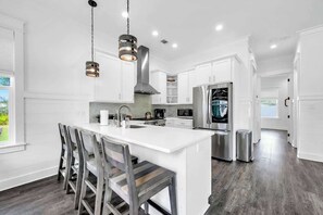 A modern kitchen with white cabinetry, a central island, stainless steel appliances, and a view to the outdoors. - The Lily by Stay on 30a (Inlet Beach)