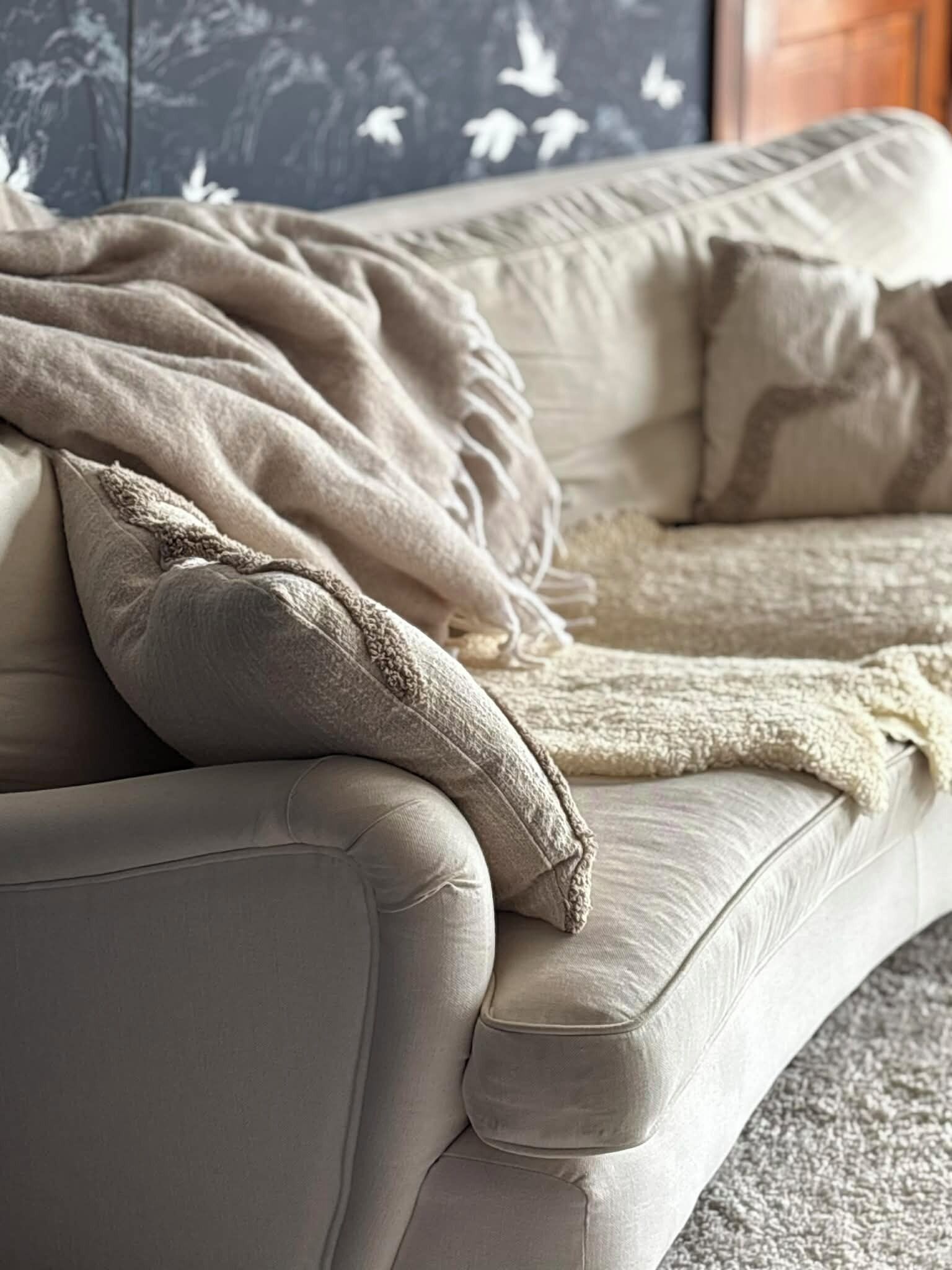 A beige sofa with a textured throw blanket and a matching pillow.