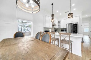 A modern kitchen with white cabinetry, a wooden dining table, and pendant lighting. - The Lotus by Stay on 30a (Inlet Beach)