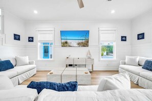 A modern hotel room with a large window, a flat-screen TV, a white console table, and two white sofas. - The Lotus by Stay on 30a (Inlet Beach)