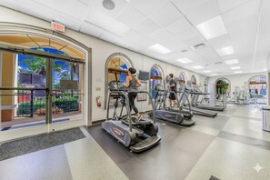 Ein Fitnessstudio mit Laufbändern, einer Trinkbrunne und Blick auf Palmen durch die Fenster.