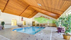 An indoor swimming pool with a wooden ceiling and tiled floor, surrounded by seating and potted plants.
