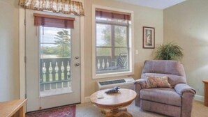 A room with a door leading to a balcony, a chair, a small round table, and a potted plant.