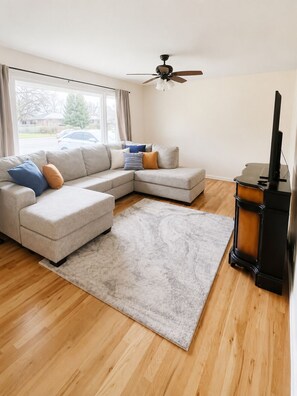 A living room with a sectional sofa, a rug, a ceiling fan, and a wood-burning stove. - Spacious 4-bedroom house Idaho Falls with AC (Idaho Falls)