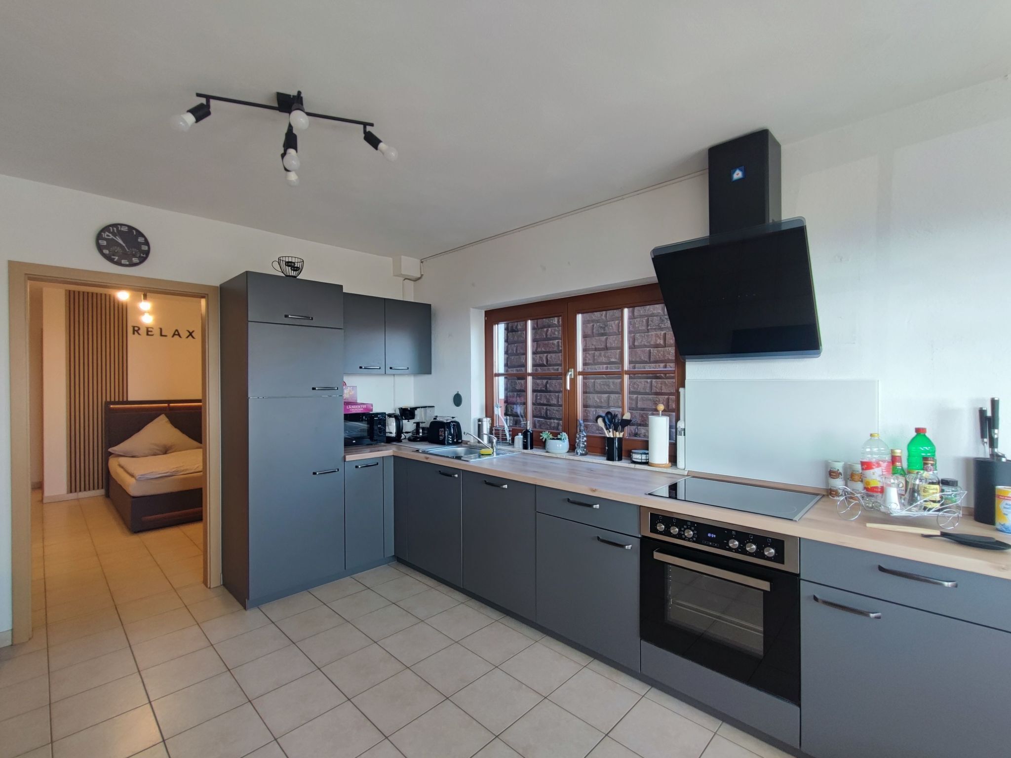 A modern kitchen with grey cabinets, a built-in oven, and a window with a brick wall.