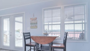 Un coin repas avec une table et des chaises, de grandes fenêtres équipées de stores et un panneau affiché sur le mur.