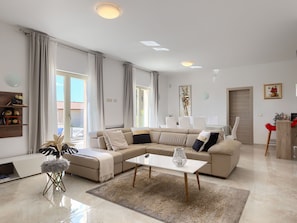Un salon moderne avec un canapé d’angle, une table basse et un coin repas avec des chaises.