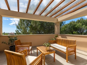 Un espace extérieur aménagé, abrité et doté de mobilier en bois et de plantes en pot.