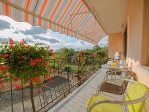 Varanda com toldo listrado, mesa com cadeiras e vista para um jardim com flores vermelhas.