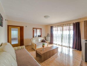 Un saló amb un sofà, una taula de centre, una cadira, un televisor i una finestra amb cortines.