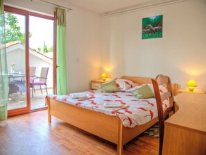 Um quarto com cama, escrivaninha, cadeira, janela e um quadro na parede.