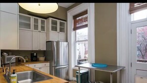 Una cocina con armarios blancos, un refrigerador de acero inoxidable, una encimera de madera, un fregadero y una ventana con vista al exterior.