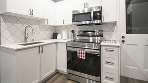 A modern kitchen with white cabinets, stainless steel appliances, and a tiled backsplash. - Executive 2-Bedroom Suite | Soundproof | Steps to Wortley Village & Vic Hospital (London)