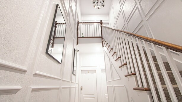 A white interior hallway with a wooden staircase and a chandelier. - Executive 2-Bedroom Suite | Soundproof | Steps to Wortley Village & Vic Hospital (London)