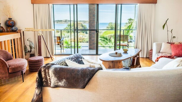 Ein geräumiges Wohnzimmer mit einer großen Glasschiebetür, die auf einen Balkon mit Meerblick führt. Im Raum befinden sich ein Sofa, ein Couchtisch und ein Sessel.