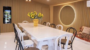 Ein moderner Essbereich mit einem langen Tisch, weißen Stühlen und einer Vase mit Sonnenblumen.