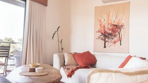Ein gemütliches Zimmer mit einer Couch, einem kleinen runden Tisch mit Schüssel und Tellern, einem Fenster mit Vorhängen und einer Wand-Klimaanlage.