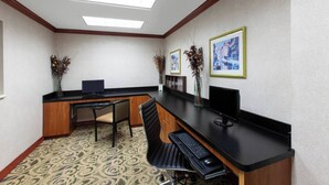 A reception area with a desk, two chairs, a computer, and framed pictures on the wall. - Hotel Willowbrook (Houston)