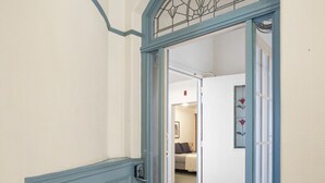 Um corredor com carpete azul, uma porta com moldura de metal e um quarto visível através de uma porta aberta.