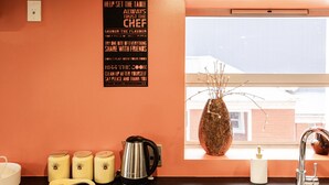 A kitchen with a wall-mounted sign listing kitchen rules, a window with a decorative vase, and kitchen appliances on the counter. - Manor Place Stays Apartment one (Dunedin)