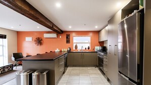 A modern kitchen with a central island, stainless steel appliances, and a decorative wall clock. - Manor Place Stays Apartment one (Dunedin)