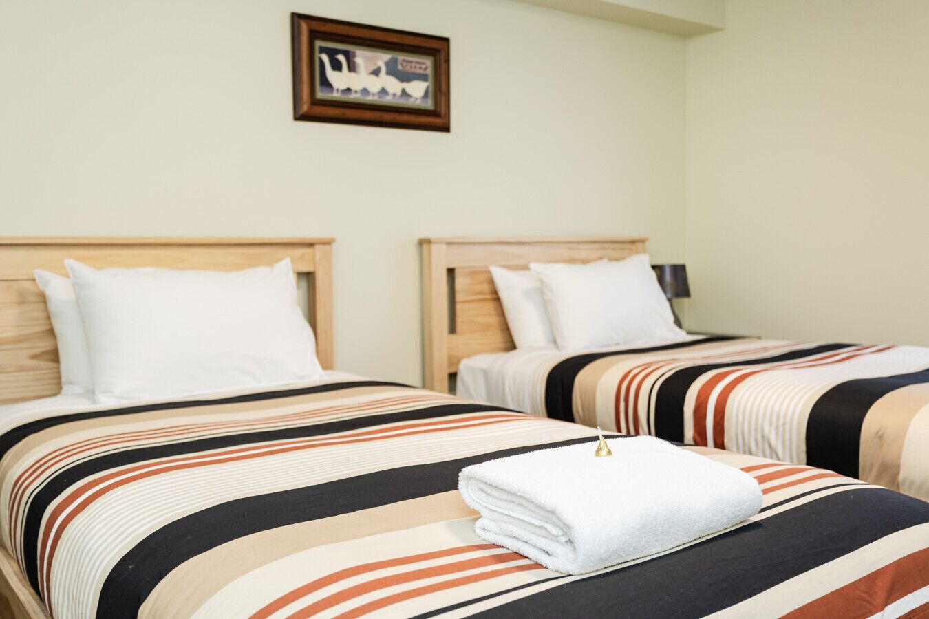 Two beds with striped bedding, a framed picture on the wall, and a folded towel on the bed.