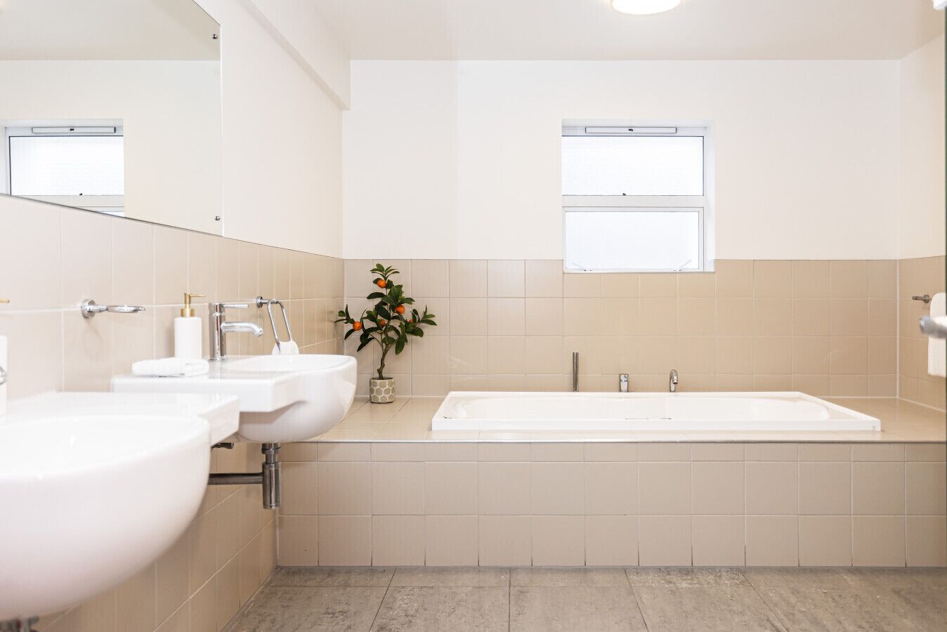 A modern bathroom with two sinks, a bathtub, and a small window.