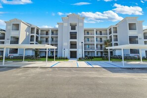 Un edificio residenziale a più piani con ingresso centrale, balconi e aree di parcheggio coperte.