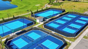 Un complexe de courts de tennis comprenant plusieurs terrains, entouré d’une clôture et situé à proximité d’un parcours de golf.