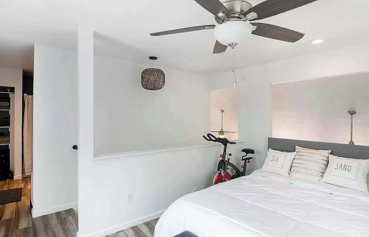 A modern bedroom with a bed, a ceiling fan, a bicycle, and a wall-mounted lamp.