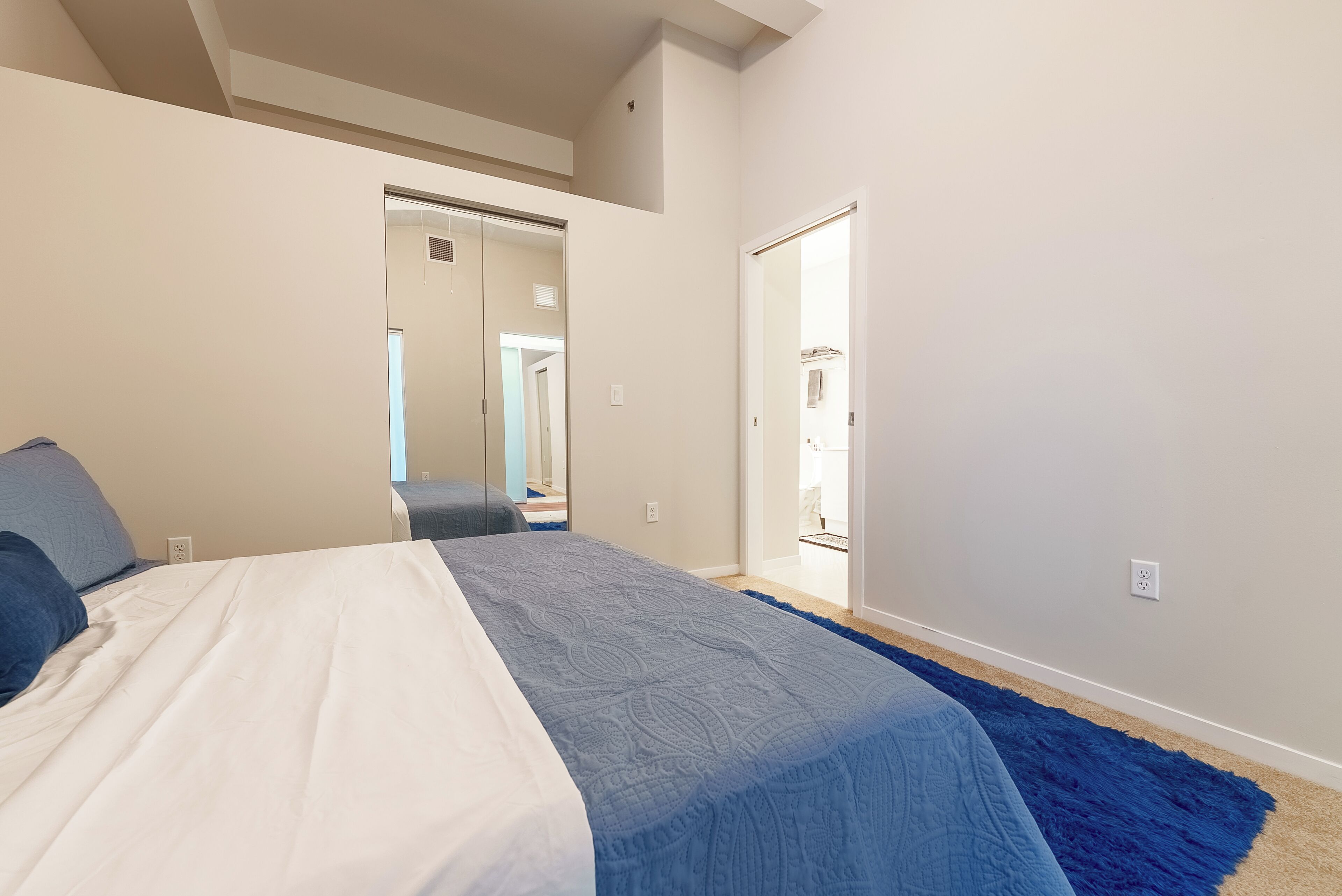 A bedroom with a bed, a blue rug, and a door leading to another room.