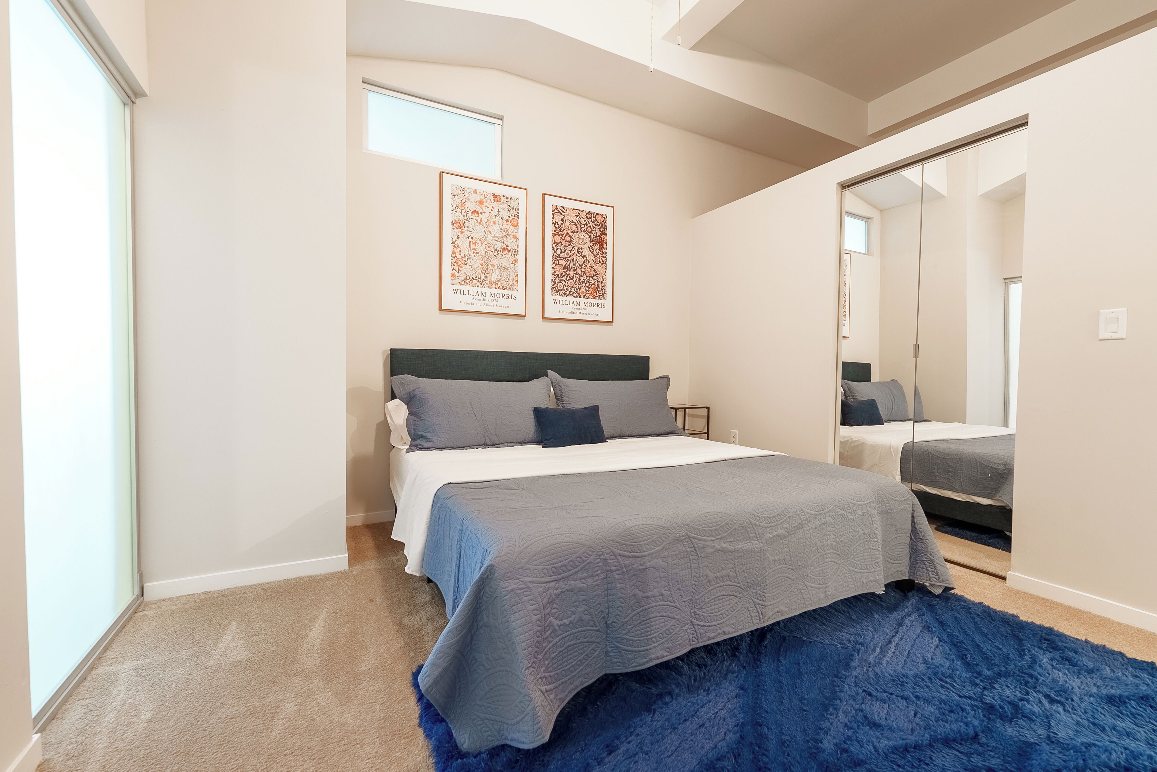 A bedroom with a bed, a large mirror, and two framed artworks on the wall.
