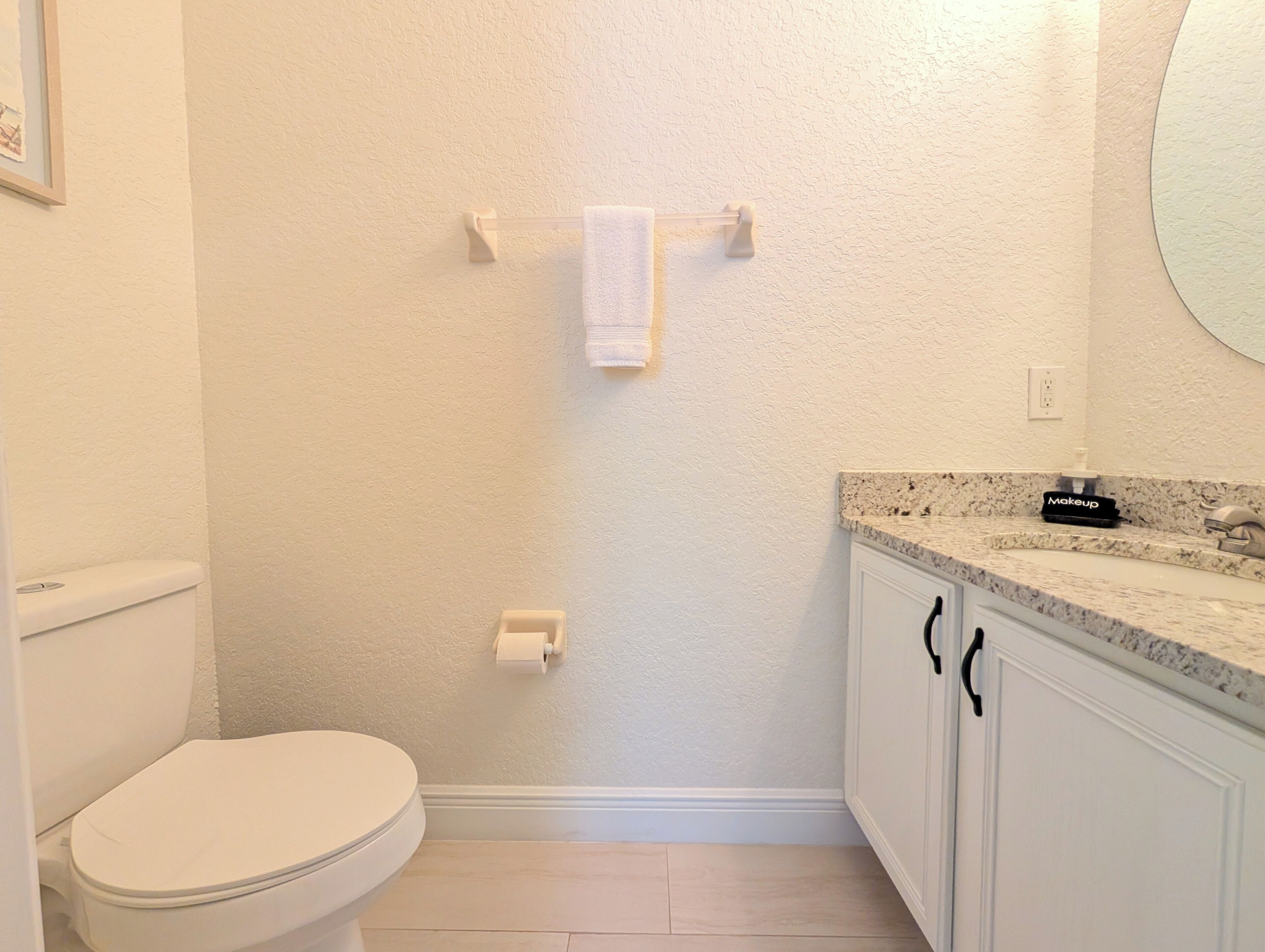 A bathroom with a toilet, a towel rack, a sink with a mirror, and a countertop with a makeup item.