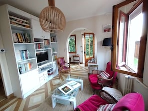 Ein Wohnzimmer mit Bücherregal, Fernseher, Couchtisch und einem roten Sofa.