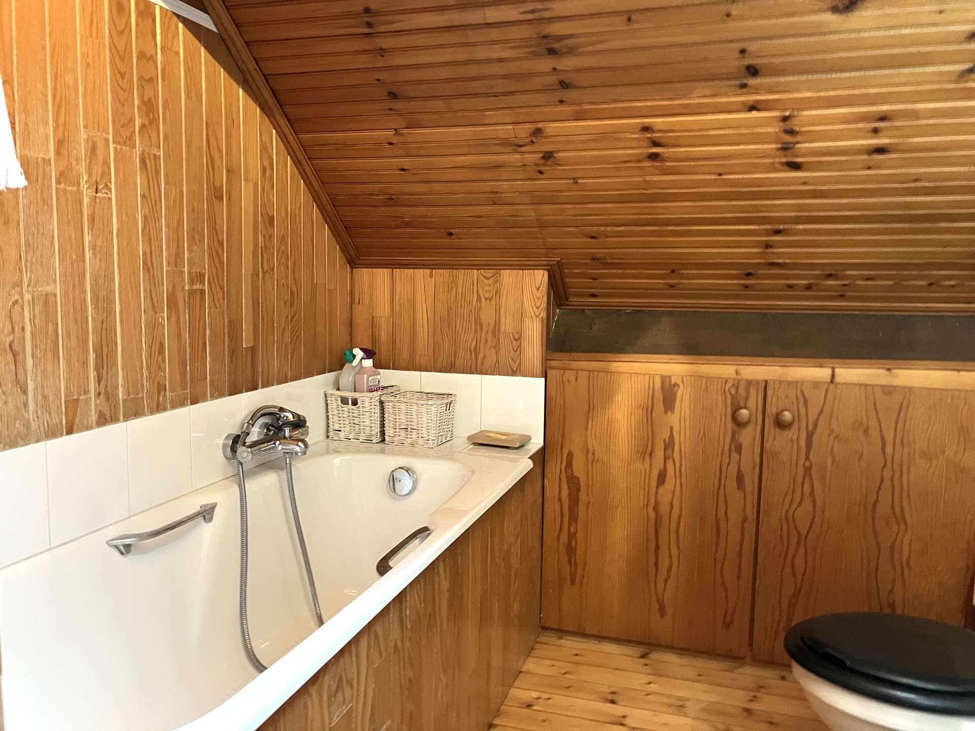 A small, wooden-paneled bathroom with a white bathtub, a toilet, and a shower.