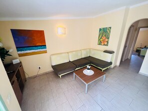 A living room with a sofa, a coffee table, and a painting of a sunset. - Gemütliches Apartment mit Pool, Nähe Strand und Stadtzentrum by Interhome (Santa Maria)