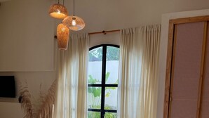 Une chambre avec un grand lit, un banc en bois, un panier en osier et un téléviseur fixé au mur.