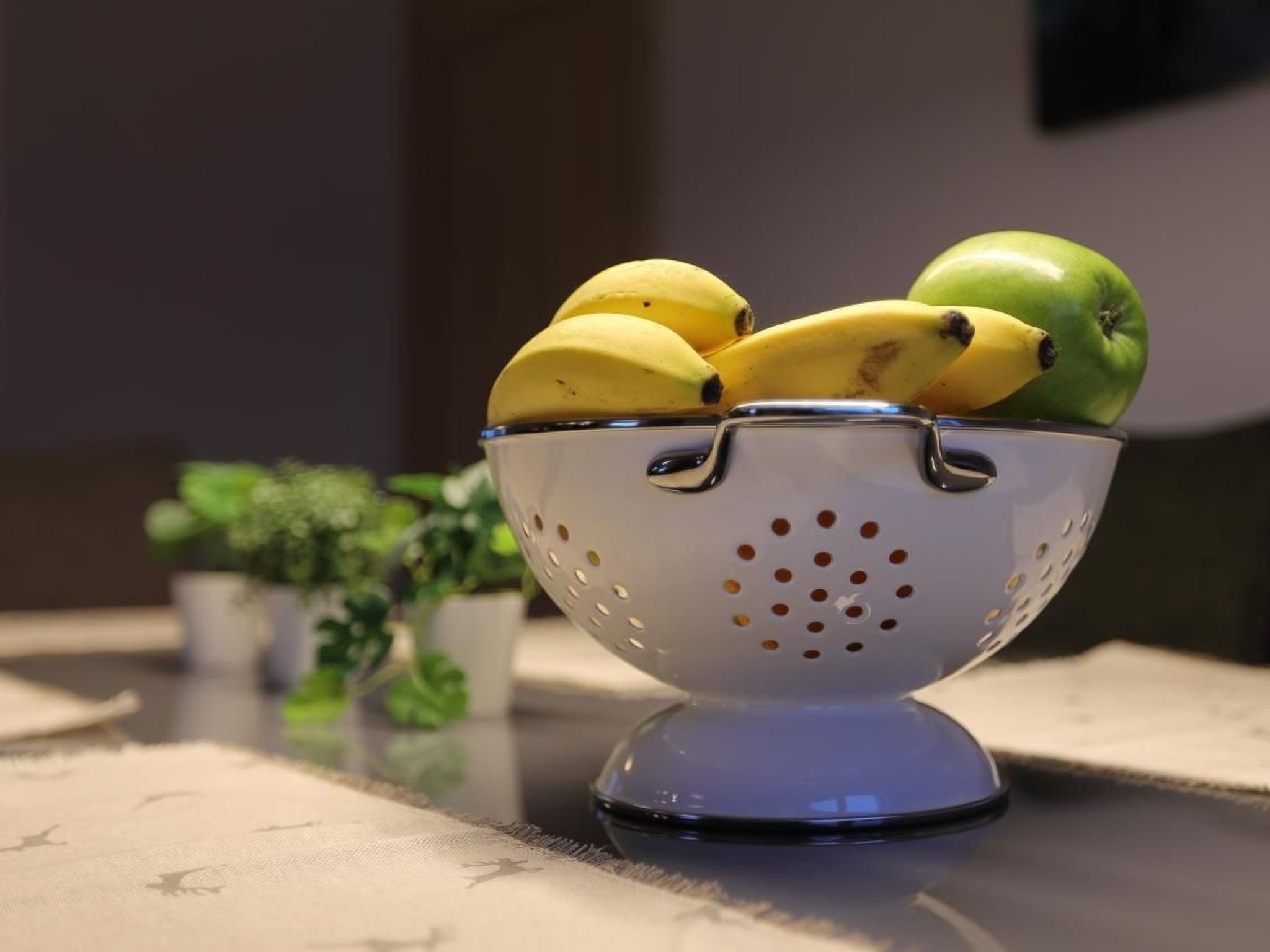 Ein Sieb mit Bananen und einem Apfel auf einem Tisch.