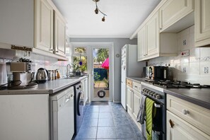 Une cuisine avec des meubles blancs, une machine à café, une cuisinière et une vue sur le jardin arrière.